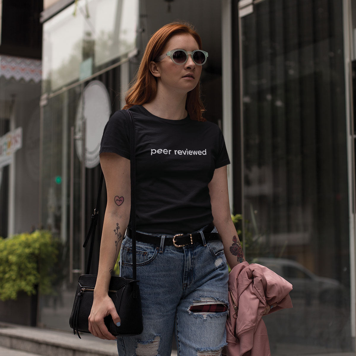 Woman wearing a black t-shirt with 'peer reviewed' text, standing on a city street.